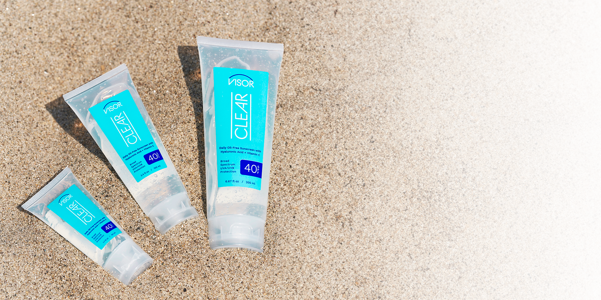 3 tubes of Visor CLEAR Sunscreen laying in sand